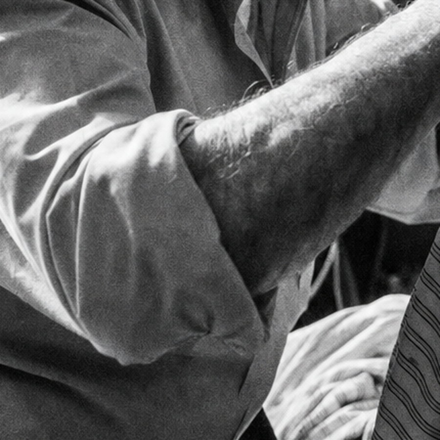 A 100% crop of a black-and-white photograph showing clustered silver grain thickening in the shadow of a shirt sleeve