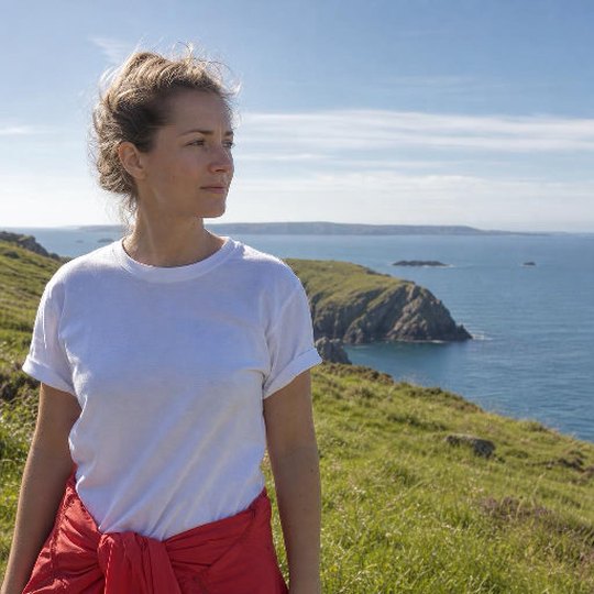 The reference photograph before printing: a woman in a white T-shirt on a grassy clifftop above the sea, clean and sharp