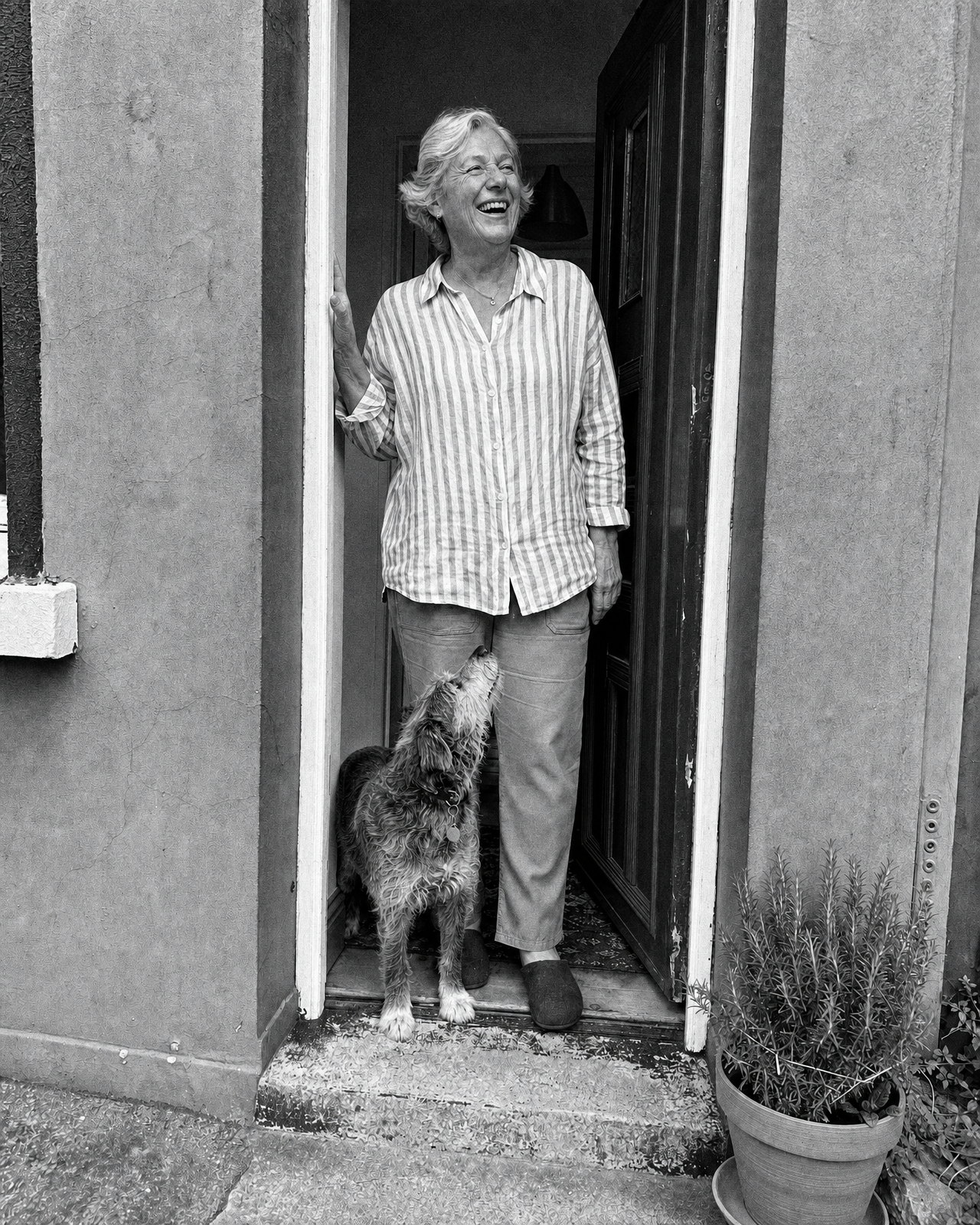 The same doorway portrait printed as Tri-X 400: black and white with deep blacks, bright unclipped highlights on the door frame and coarse sharp grain across the greys