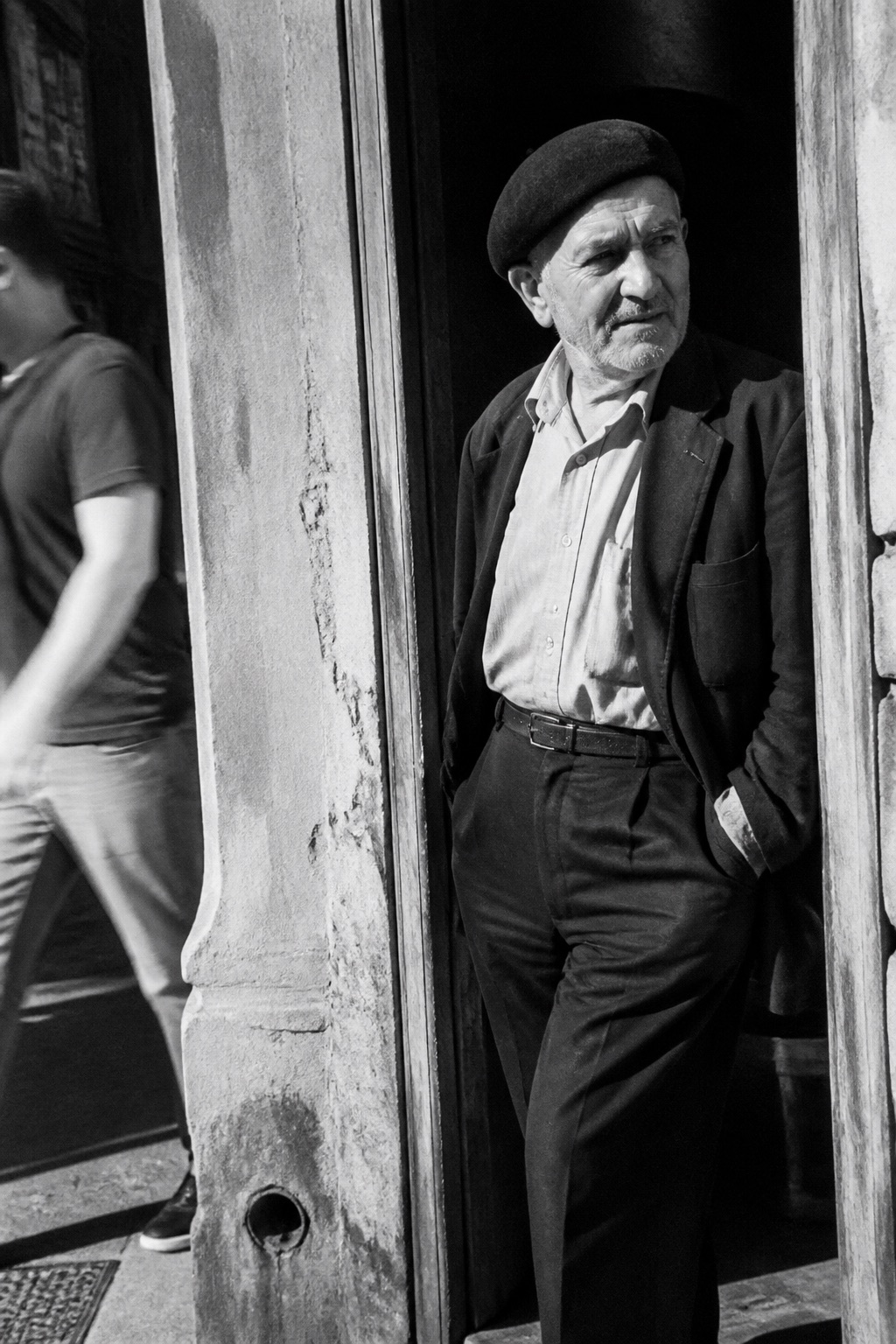 An older man in a flat cap standing in a doorway, in high-contrast black and white with sharp film grain